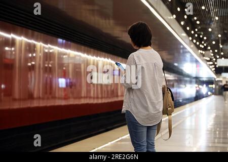 Woman with smartphone standing on background of arriving train in a metro Stock Photo