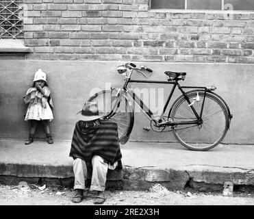 Chia, Colombia:  c. 1960 A man sitting on the curb on a street in Chia just north of Bogota in Colombia. Stock Photo