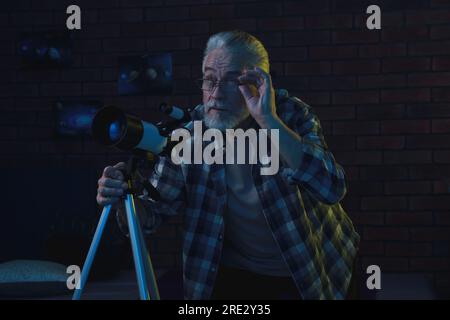 Senior man using telescope to look at stars in room Stock Photo