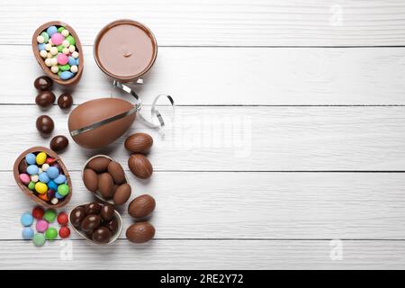 Delicious chocolate eggs, paste and candies on white wooden table, flat lay. Space for text Stock Photo