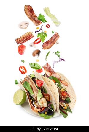 Delicious tacos. Ingredients falling into tortillas on white background Stock Photo