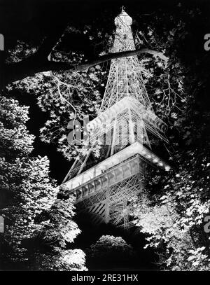 Paris, France:  c. 1962 The Eiffel Tower at night seen through the trees. Stock Photo