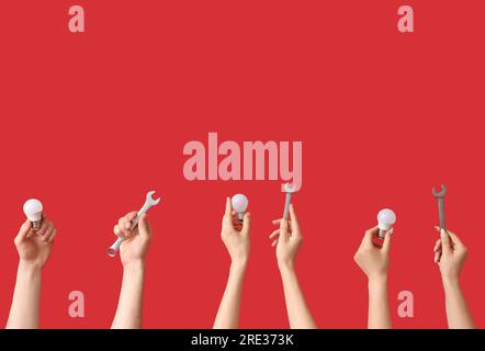 Electrician hands with light bulbs and wrenches on red background Stock Photo