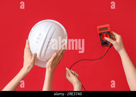 Electrician hands with hardhat and multimeter on red background Stock Photo