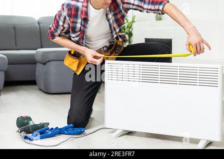 Workman mounting water heating radiator near the window in the white renovated living room, Image with copy space Stock Photo