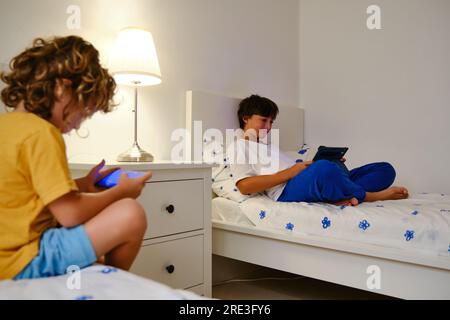Brothers using gadgets in bedroom Stock Photo