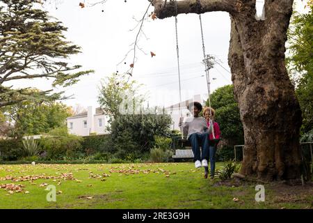 Happy african american mother and son swinging on tree swing in garden, copy space Stock Photo