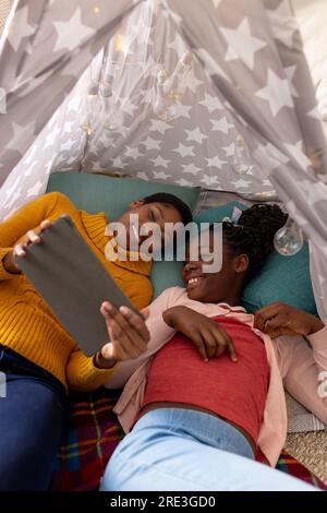Happy african american mother and daughter using tablet in tent at home Stock Photo