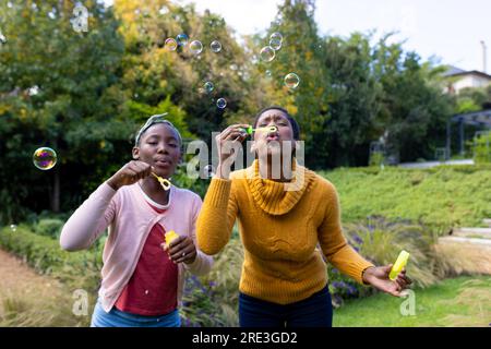 African american mother and daughter blowing bubbles in garden at home Stock Photo