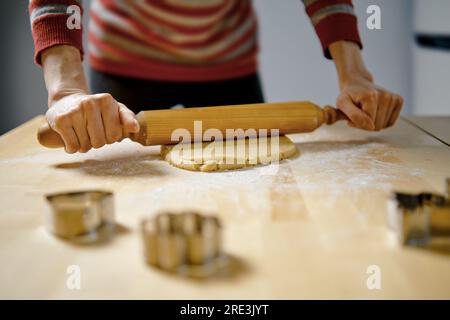 Unrecognizable woman rolls out ginger dough with rolling pin on kitchen table (low angle view with selective focus photo) Stock Photo