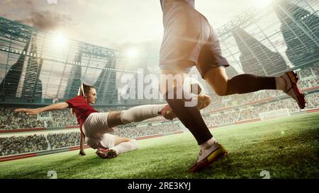 Dynamic image of female football players in motion during match, game. Woman hitting ball and falling down. 3d arena, blurred audience Stock Photo