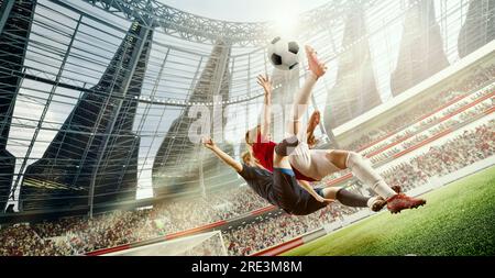 Tense game moment. Dynamic image of two women, football players in motion, hitting ball in jump during match on 3D open air stadium Stock Photo