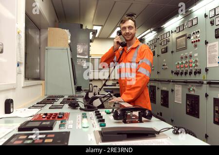 Young marine specialist performing radio checks in engine control room. Stock Photo