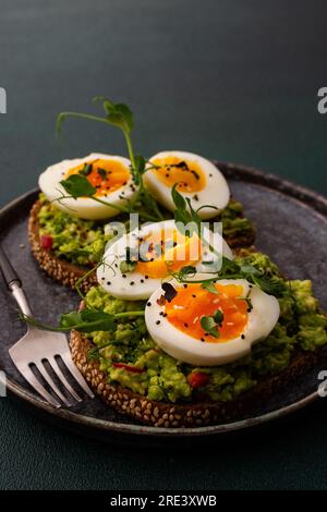 Sandwiches with rye bread and guacamole, with boiled eggs and microgreens of peas and radishes and sesame seeds, a plate with sandwiches close-up Stock Photo