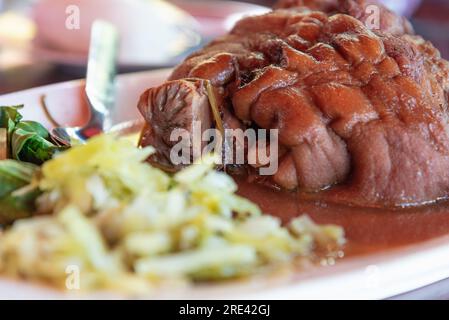 Stewed pork leg with pickled vegetables and green kale on white plate Stock Photo