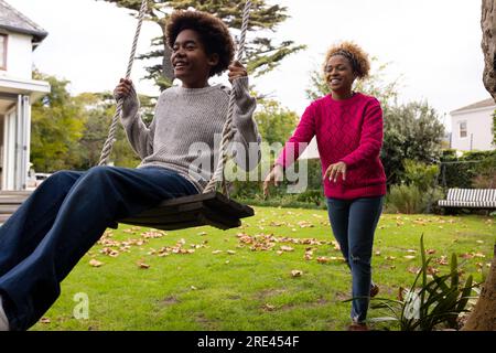 Happy african american mother and son swinging on tree swing in garden Stock Photo