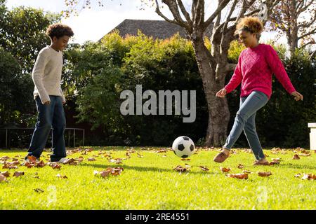 Happy african american mother and son playing football in garden Stock Photo