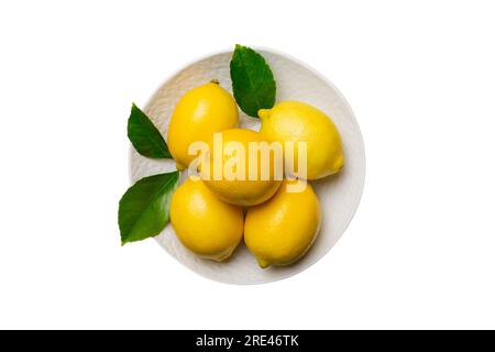 Fresh cutted lemon and whole lemons over round plate isolated on white background. Food and drink ingredients preparing. healthy eating theme top view Stock Photo