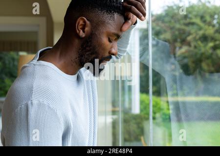 Thoughtful african american man leaning against window at home Stock Photo