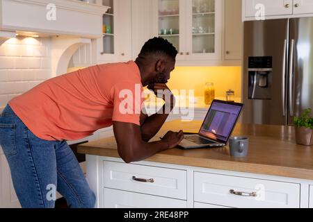 African american man using laptop in white kitchen Stock Photo