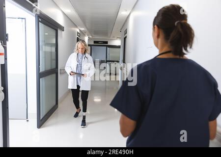 Caucasian female doctors using tablet walking in corridor at hospital Stock Photo