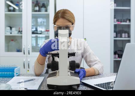 Serious and focused female researcher working with microscope inside laboratory, mature and experienced scientist studying and testing medicine. Stock Photo