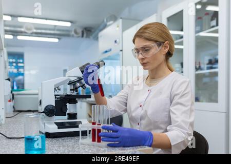 Serious and focused female researcher working with microscope inside laboratory, mature and experienced scientist studying and testing medicine. Stock Photo