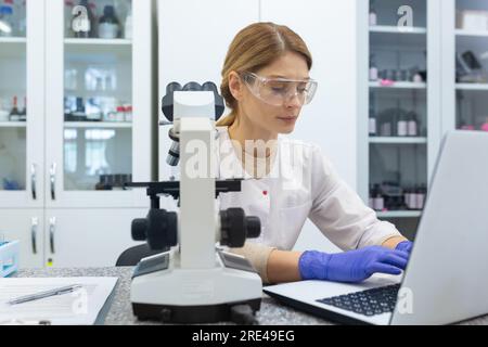 Serious and focused female researcher working with microscope inside laboratory, mature and experienced scientist studying and testing medicine. Stock Photo