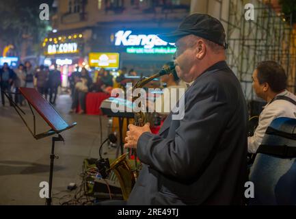 A Vietnamese man plays saxophone in a band in the street at night in Hanoi, Vietnam. The area around Hoan Kiem Lake in the centre of the city becom,es Stock Photo