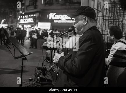 A Vietnamese man plays saxophone in a band in the street at night in Hanoi, Vietnam. The area around Hoan Kiem Lake in the centre of the city becom,es Stock Photo