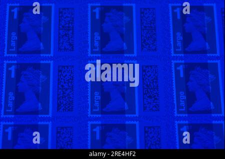 England, 25th July 2023: Fake Royal Mail 1st Class Large Letter Stamps under UV light. - Counterfeit Royal Mail barcoded stamps are for sale on eBay at a fraction of the genuine price. Sheets of 50 stamps are for sale as low as 15 pounds (GBP) and to the unsuspecting eye look real. However under UV light, small differences can be seen. Credit: Stop Press Media/Alamy Live News Stock Photo