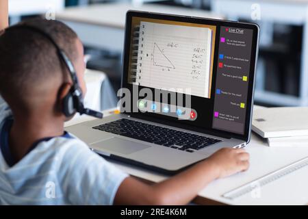Rear view of african american boy wearing headphones using laptop and studying at home Stock Photo