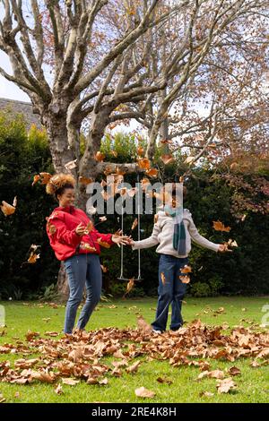 Happy african american mother and son throwing leaves in garden Stock Photo