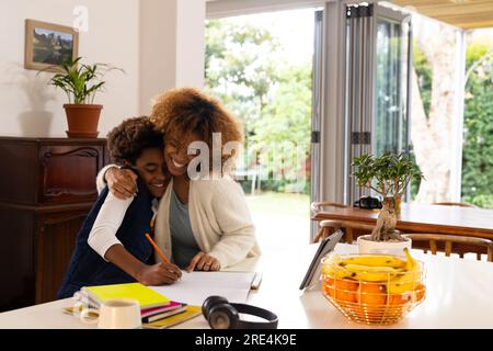 Happy african american mother and son sitting at table, doing homework Stock Photo