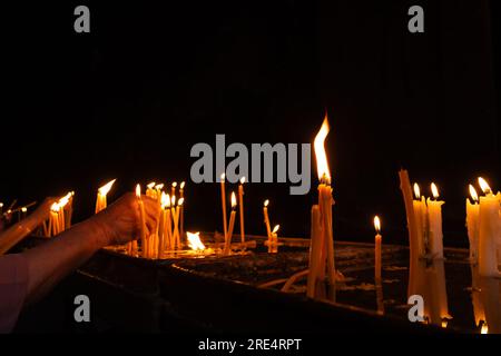 Women's hands light candles in a monastery, close-up Stock Photo
