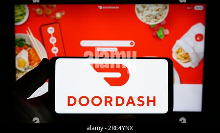 Person holding smartphone with logo of US food delivery company DoorDash Inc. on screen in front of website. Focus on phone display. Stock Photo