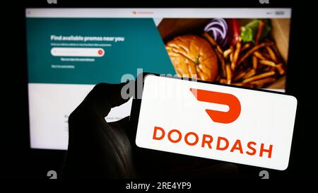 Person holding cellphone with logo of US food delivery company DoorDash Inc. on screen in front of business webpage. Focus on phone display. Stock Photo