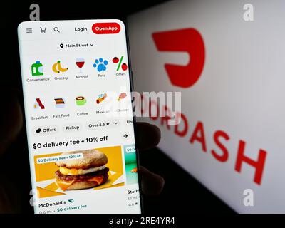 Person holding mobile phone with web page of US food delivery company DoorDash Inc. on screen in front of logo. Focus on center of phone display. Stock Photo