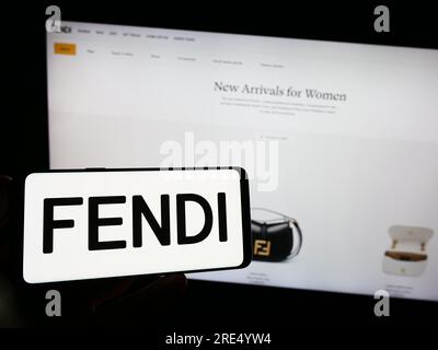 Person holding smartphone with logo of Italian fashion company Fendi S.r.l. on screen in front of website. Focus on phone display. Stock Photo