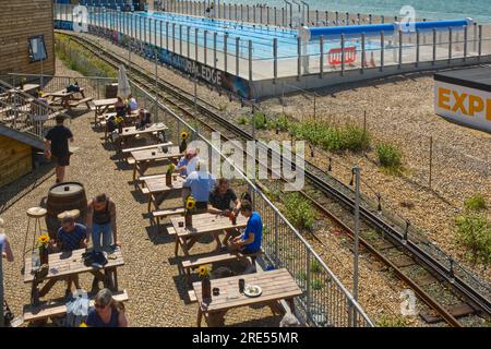 New swimming poo, cafe and restaurant on shingle beach at Brighton, East Sussex, England. With people in pool and cafe. Stock Photo