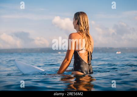 Surfer woman sitting on surfboard and waiting waves. Woman with surfboard in ocean Stock Photo