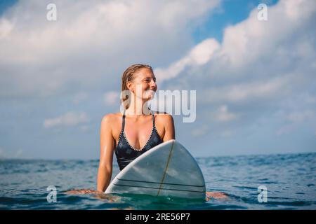 Surfer woman sitting on surfboard and waiting waves. Woman with surfboard in ocean Stock Photo