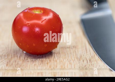 Chopping tomato on wooden table. Red round lucid tomato with metal knife on right side Stock Photo