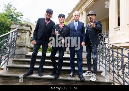 Hanover, Germany. 25th July, 2023. Matthias Jabs (l-r), band member of the 'Scorpions', Klaus Meine, band member of the 'Scorpions', Stephan Weil (SPD), Minister President of Lower Saxony, and Rudolf Schenker, band member of the 'Scorpions', stand in the garden of the guest house of the state government after receiving the Grand Cross of Merit of the Order of Merit of Lower Saxony. Three band members of the rock band 'Scorpions' are honored for their music as well as their honorary commitment in Lower Saxony. Credit: Michael Matthey/dpa/Alamy Live News Stock Photo