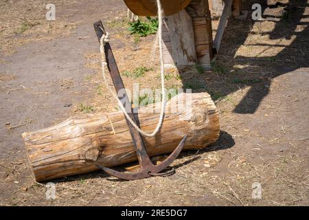 Old rusty ship anchor, iron cat propped up against a log Stock Photo