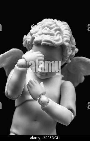 Sad cherub with facepalm gesturing. Angel figurine holding his head in hands on black background. Ashamed, sad, depressed, confused, worried concept Stock Photo