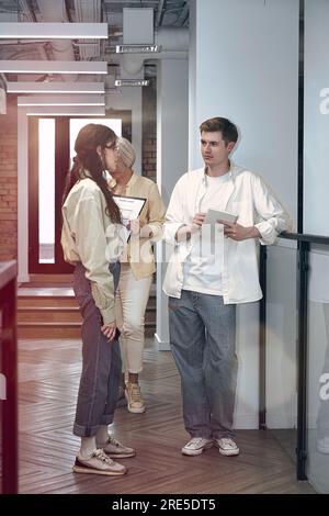 A young man and woman workers talking while standing in the office hall with their colleague in the background. The startup, coworking, management Stock Photo