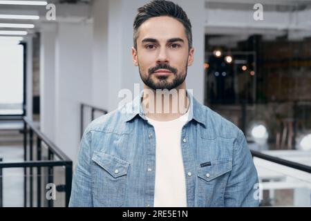 Creative young handsome man looking at the camera with a modern coworking space in the background. The startup, coworking, and management concept Stock Photo