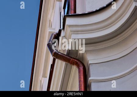 shiny new copper rain water leader, downspout or down pipe detail. home renovation and construction closeup. textured stucco. roof edge. blue sky. Stock Photo