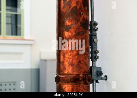 shiny new copper rain water leader, downspout or down pipe detail. lightning protection grounding rod. home renovation, construction. stucco elevation Stock Photo